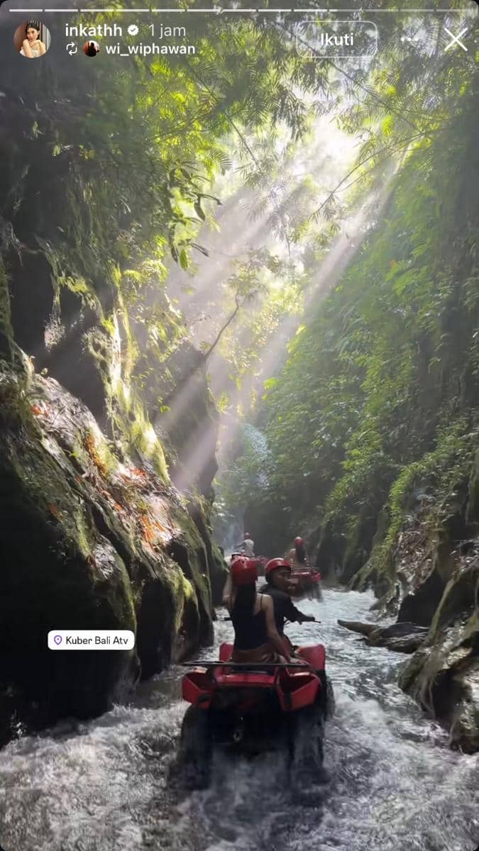 Beberapa orang mengendarai ATV merah melewati sungai sempit di antara tebing hijau dengan sinar matahari menembus pepohonan di Bali.