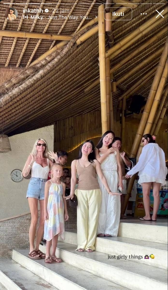 Sekelompok perempuan dan anak kecil berpose di tangga bangunan bambu bergaya tropis saat liburan di Bali.
