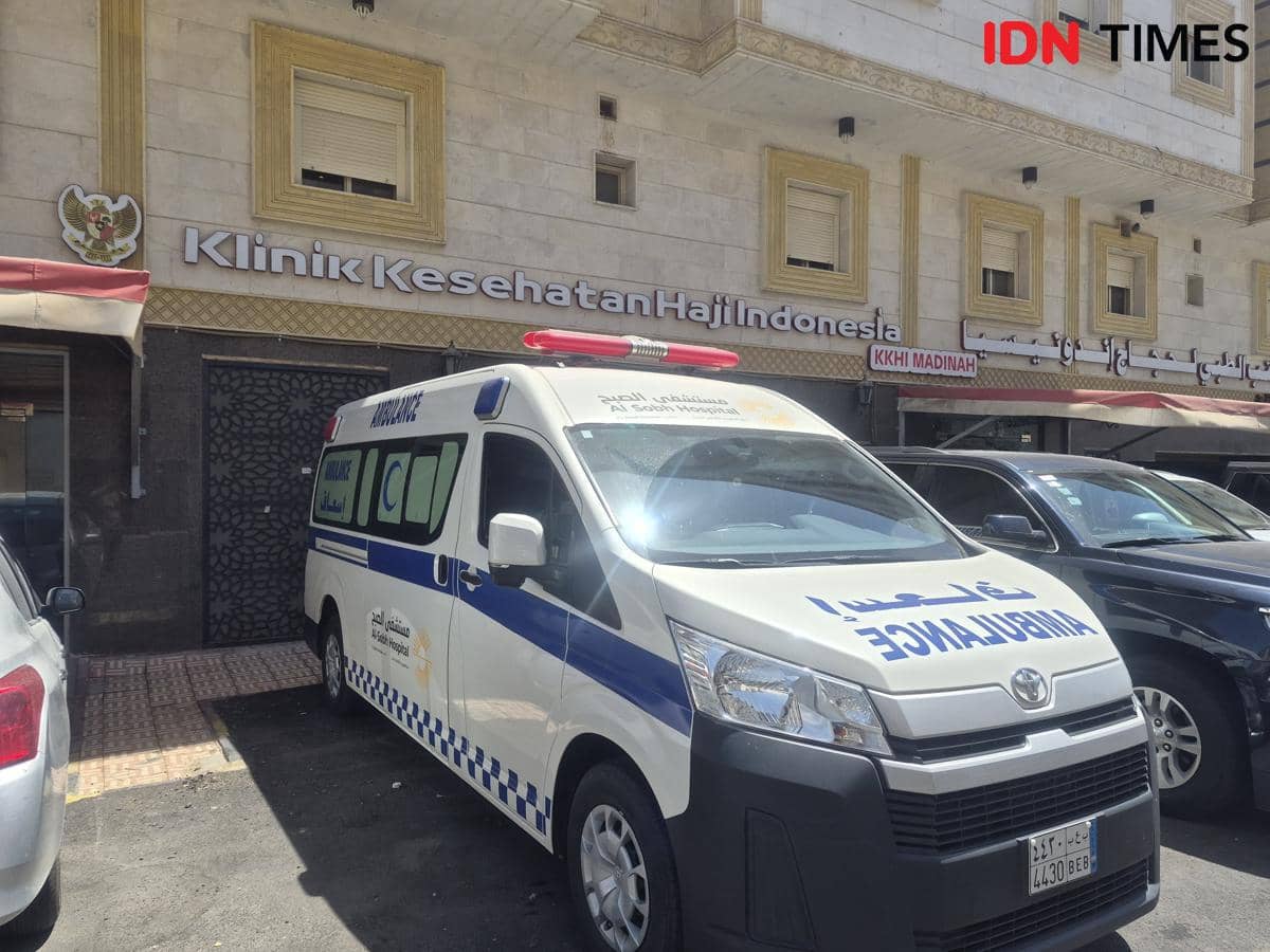 Ambulans berwarna putih dan biru terparkir di depan gedung Klinik Kesehatan Haji Indonesia dengan papan nama terlihat jelas.