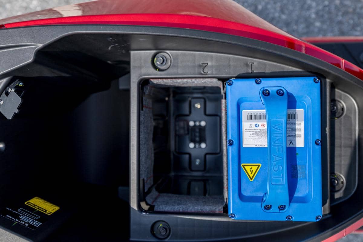 Baterai motor listrik VinFast berwarna biru terpasang di dalam kompartemen bawah jok kendaraan dengan bodi berwarna merah.