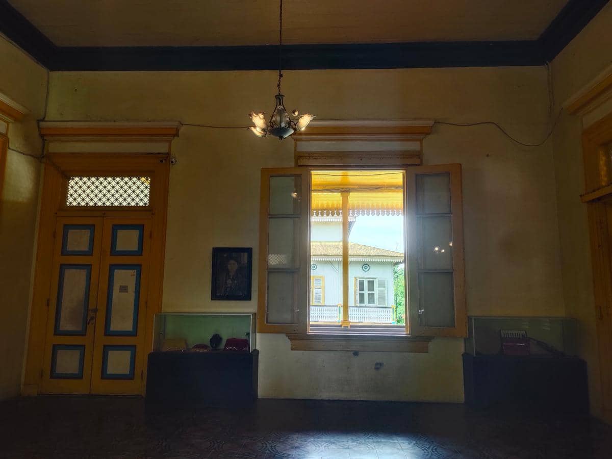 Ruang dalam istana dengan dinding kuning, jendela besar terbuka, pintu kayu berwarna biru dan kuning, serta pajangan benda bersejarah.
