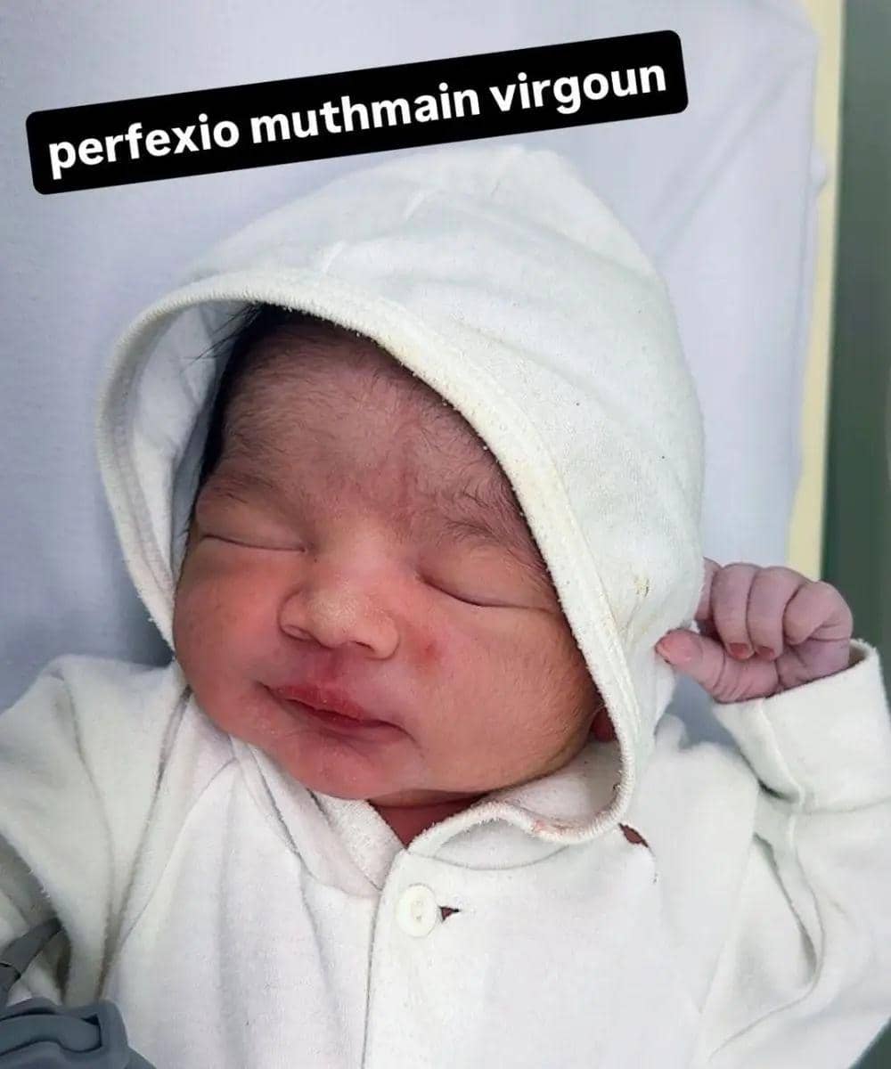 Bayi baru lahir mengenakan pakaian dan tudung berwarna putih sedang berbaring dengan mata tertutup di ruang bersalin.