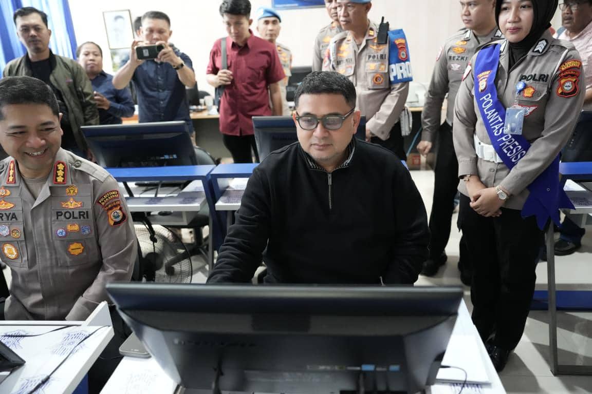Seorang pria duduk di depan komputer mengikuti ujian teori di ruang Satpas, didampingi beberapa petugas polisi yang mengenakan seragam.