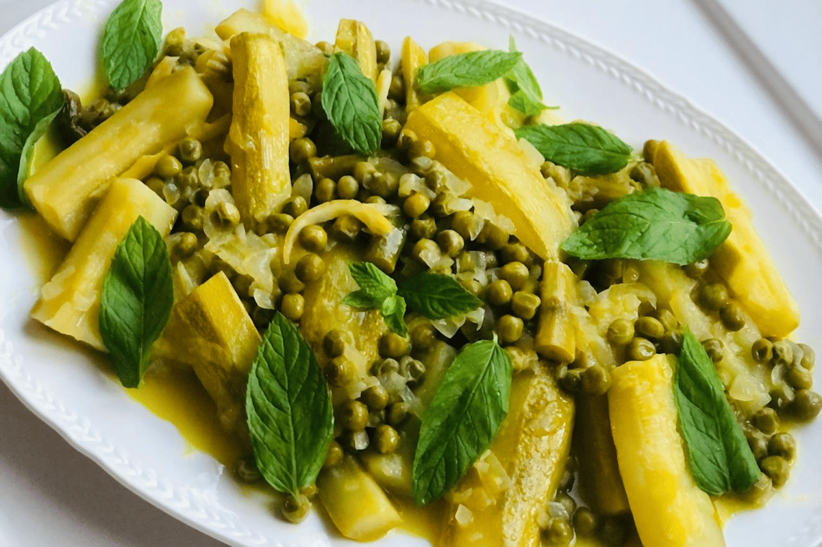 Hidangan pasta e piselli dengan potongan zucchini, kacang polong hijau, dan daun mint segar disajikan di atas piring putih.