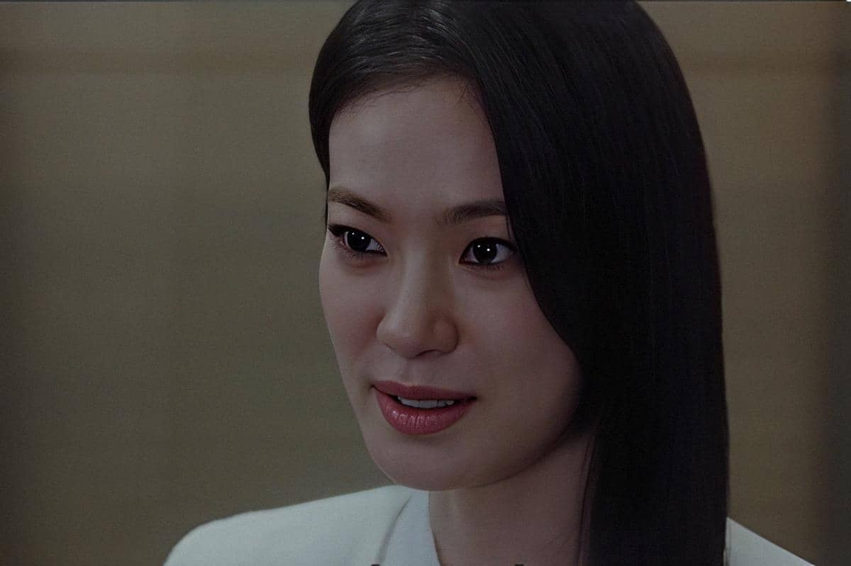 Seorang wanita berambut panjang hitam tersenyum tipis dalam cuplikan drama Sold Out on You dengan latar ruangan netral.