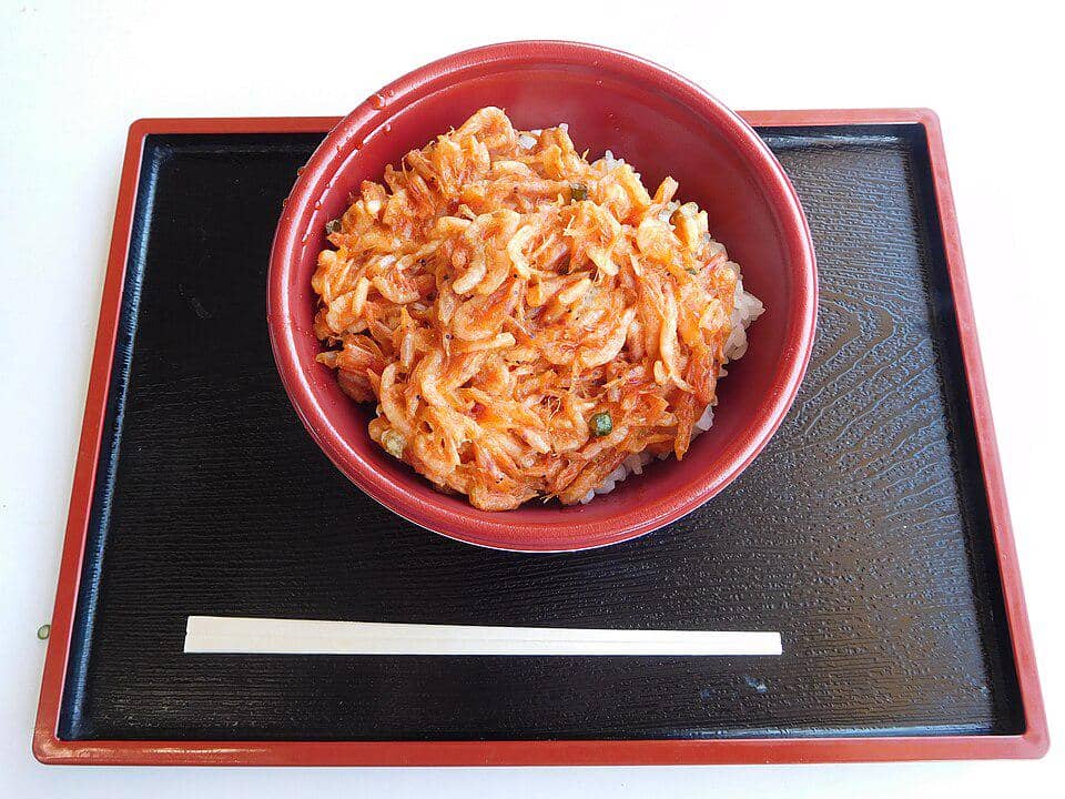 Semangkuk donburi berisi nasi putih dengan topping kakiage berwarna keemasan disajikan di atas nampan hitam dengan sumpit kayu.