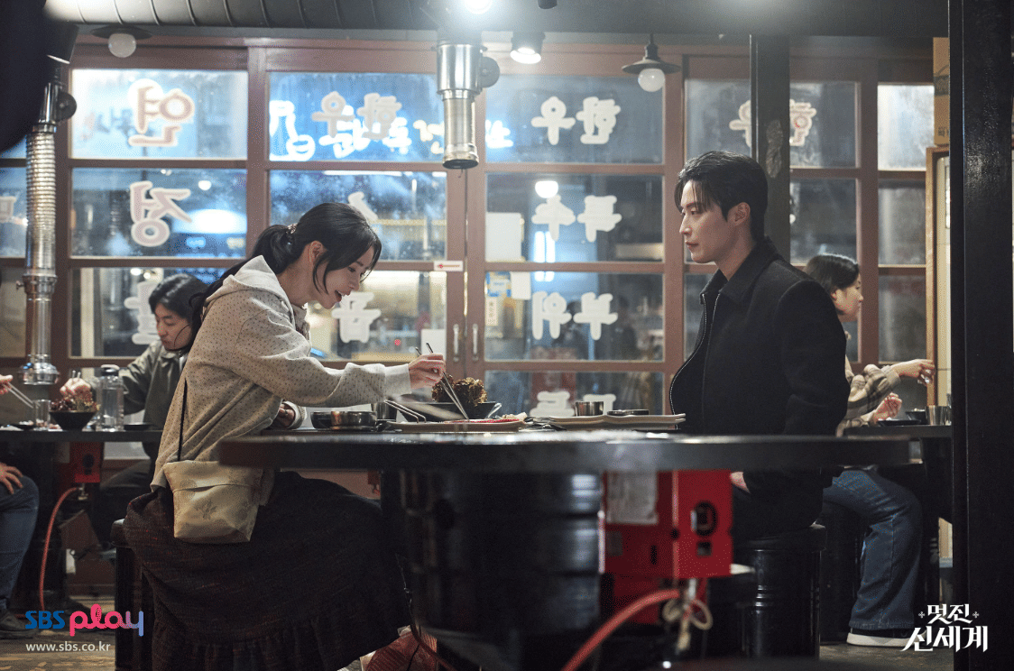 Dua karakter duduk berhadapan di restoran bergaya Korea dengan suasana hangat dan pencahayaan lembut dalam drama My Royal Nemesis.