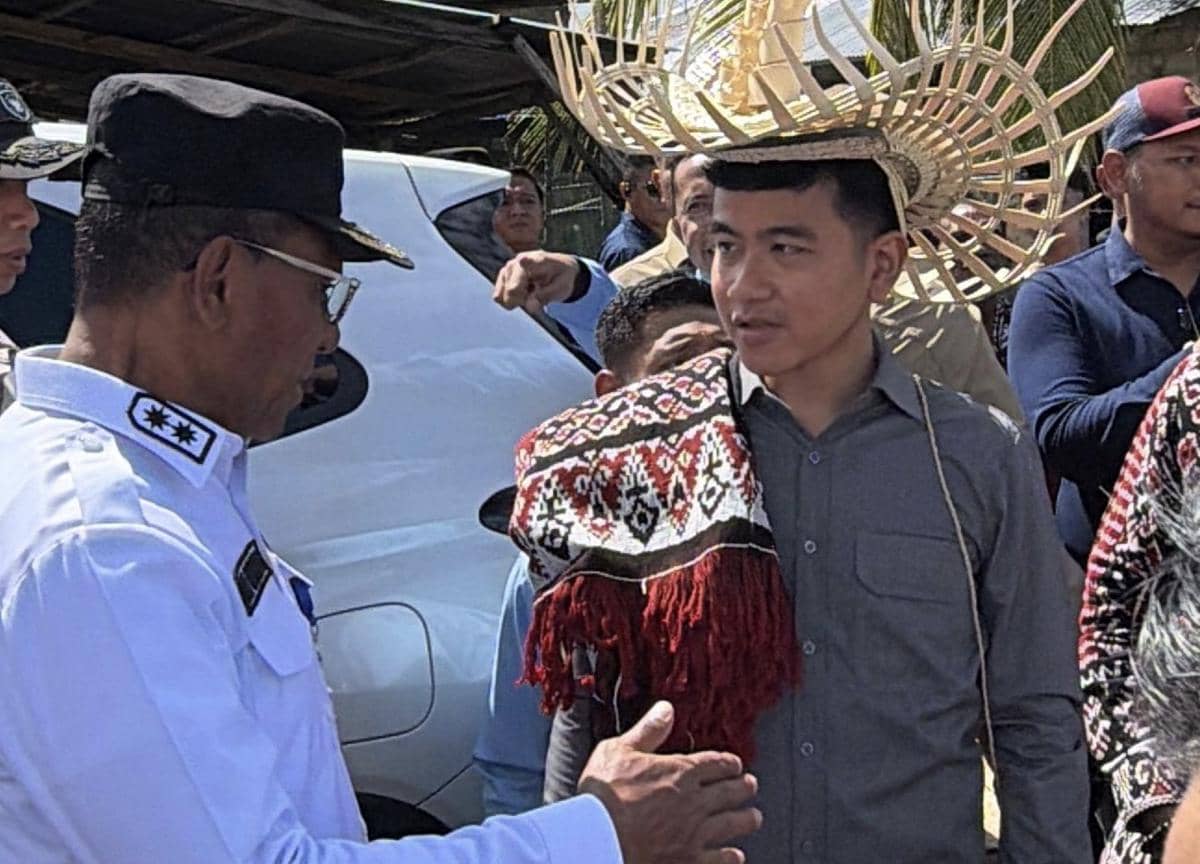 Seorang pria mengenakan kemeja abu-abu dan topi tradisional berbentuk anyaman berbicara dengan pejabat berseragam putih di Rote, NTT.