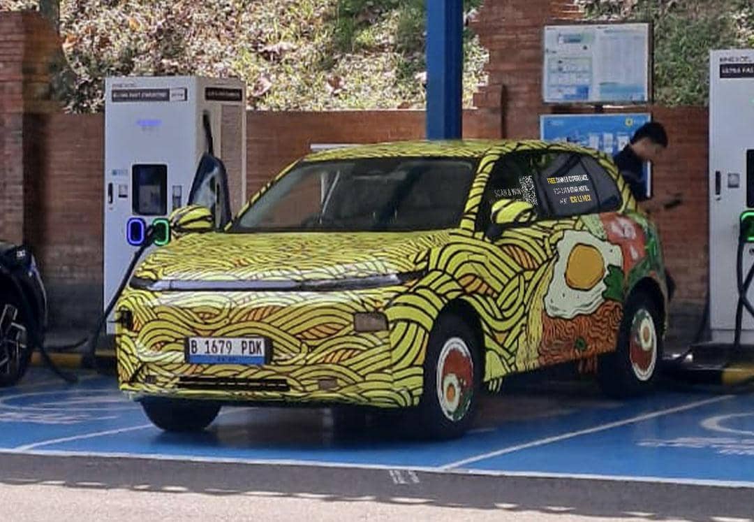 Mobil listrik dengan desain unik bergambar mi dan telur sedang mengisi daya di stasiun pengisian kendaraan listrik di Jakarta.