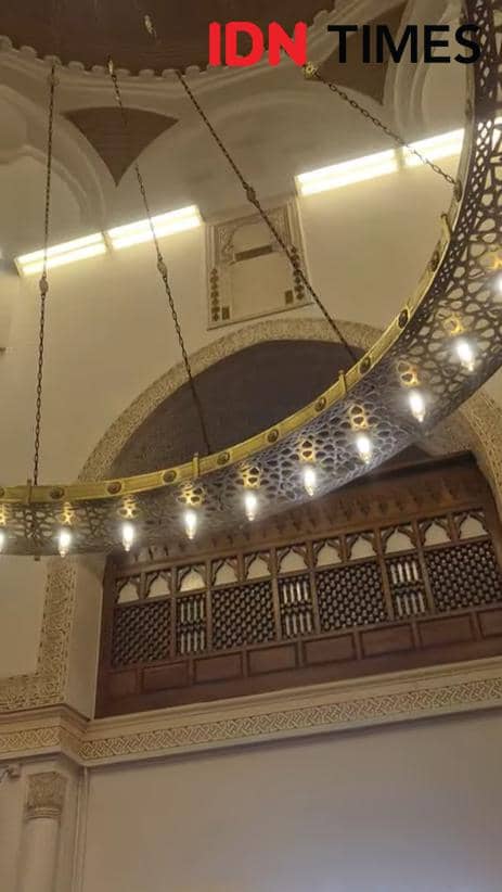 Ukiran mihrab dengan arah ke Masjid Al Aqsa di Yerusalem, menampilkan detail arsitektur islami dan lampu gantung besar.