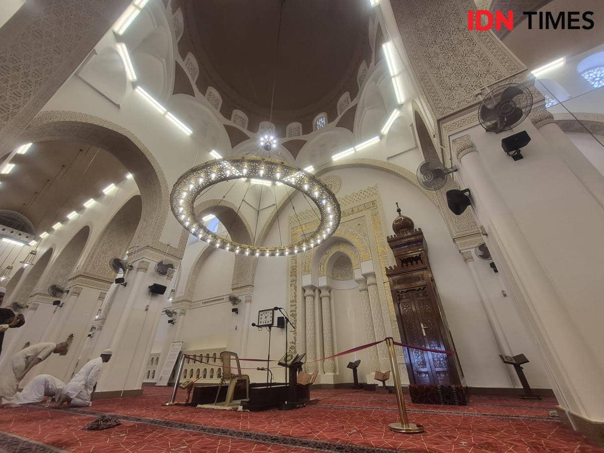 Interior masjid Qiblatain dengan mihrab menghadap ke arah Ka'bah di Makkah, menampilkan arsitektur islami dan jamaah yang beribadah.