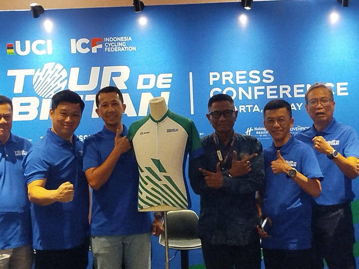 Beberapa pria berpose bersama jersey resmi Tour de Bintan 2026 saat konferensi pers dengan latar belakang biru bertuliskan logo acara.