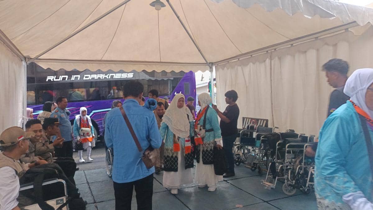 Calon jemaah haji asal Pinrang tiba di Asrama Haji Sudiang, beberapa di antaranya mengenakan pakaian seragam haji dan berbincang di bawah tenda.