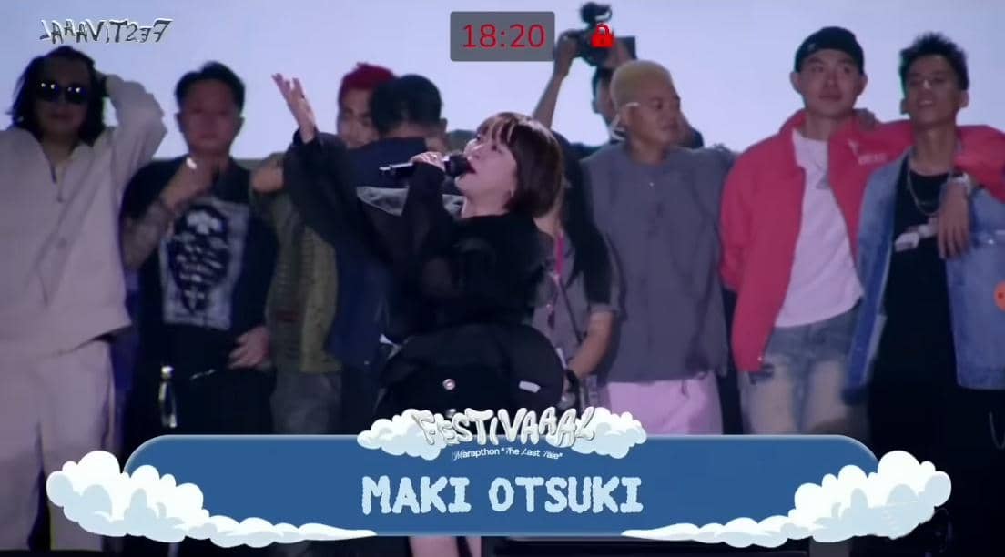 Seorang penyanyi tampil di atas panggung Festival Marapthon: The Last Tale sambil memegang mikrofon, dikelilingi beberapa orang di belakangnya.