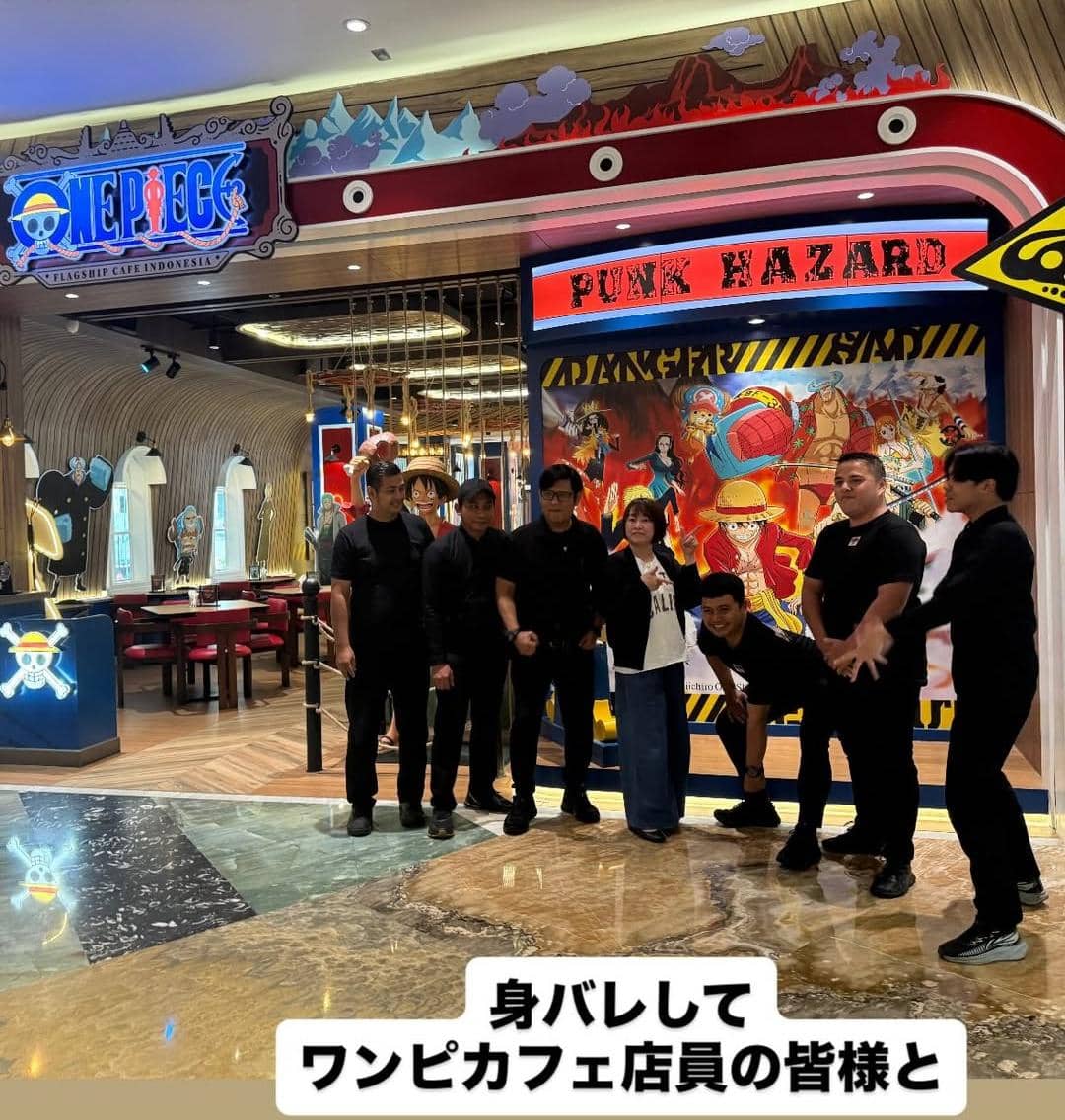 Seorang perempuan berpose bersama beberapa pria di depan One Piece Cafe Indonesia dengan latar dekorasi bertema anime One Piece.