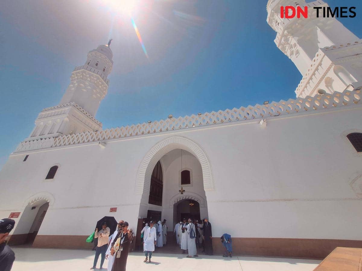 Masjid Qiblatain di Madinah dengan dua menara putih menjulang dan pengunjung yang keluar masuk di bawah sinar matahari cerah.