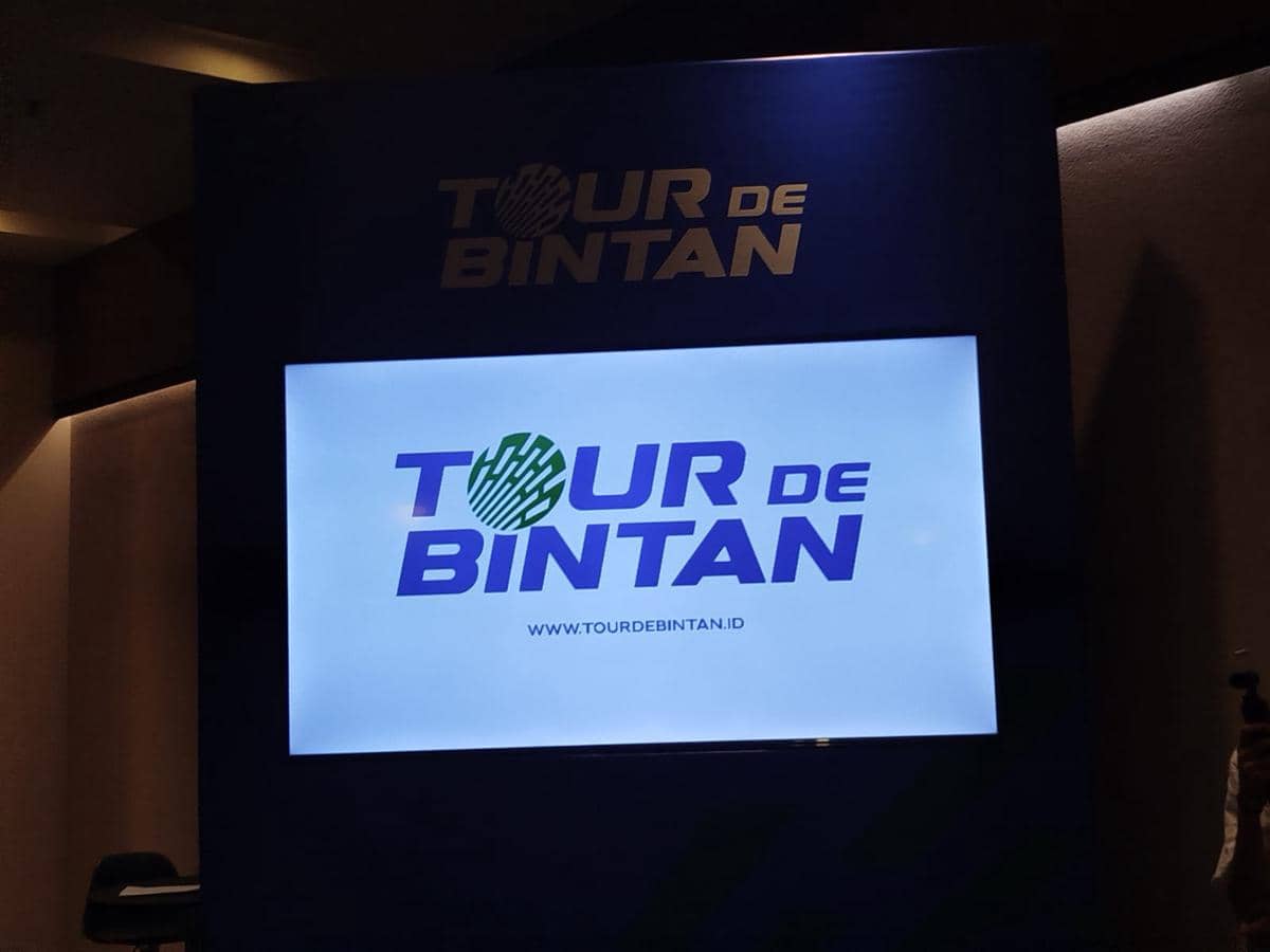 Layar menampilkan logo dan situs resmi Tour de Bintan dengan latar biru dalam acara peluncuran edisi 2026.