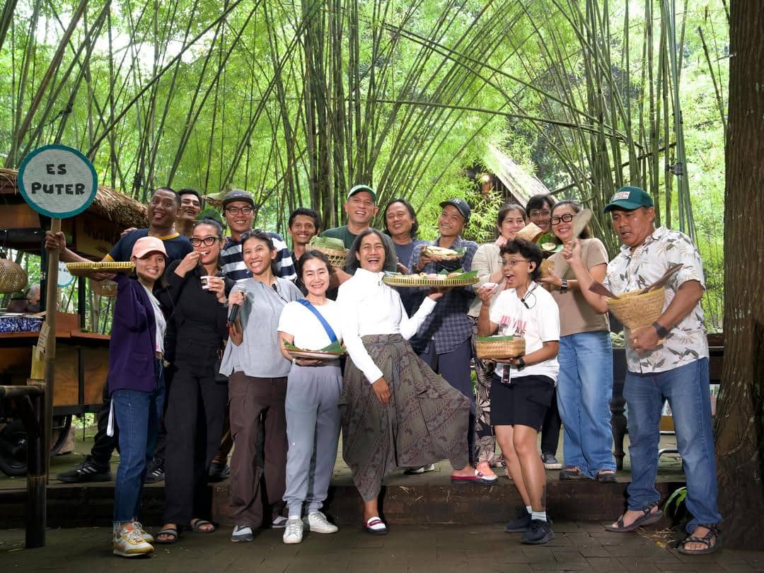 Kru film Berbagi Suami 2 berpose bersama di area bambu hijau sambil memegang makanan dan minuman tradisional dengan suasana ceria.