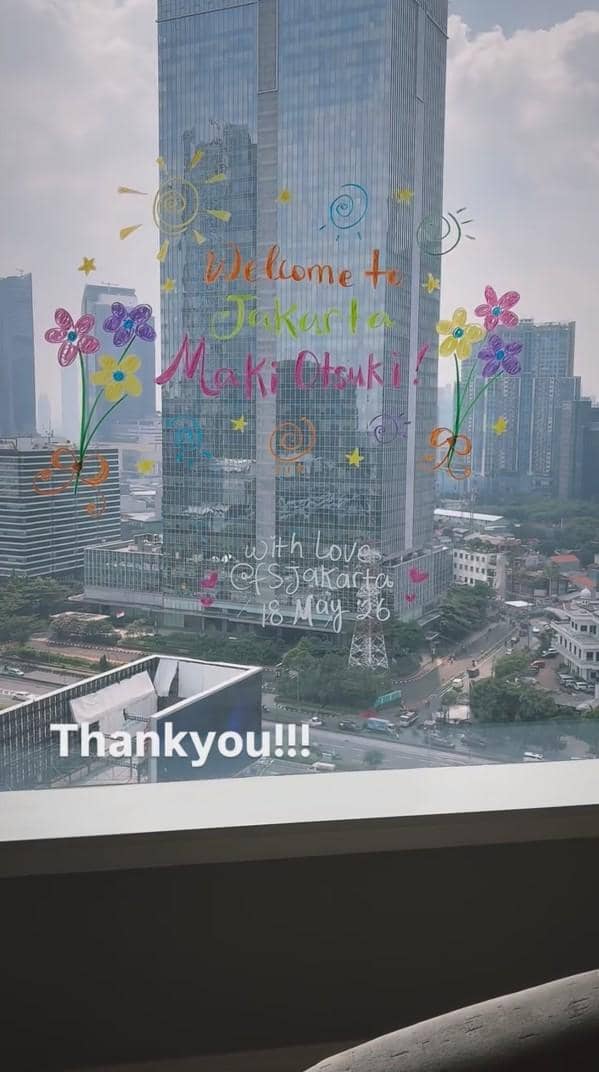 Pemandangan gedung pencakar langit di Jakarta dengan tulisan sambutan berwarna di kaca bertuliskan 'Welcome to Jakarta Maki Otsuki'.