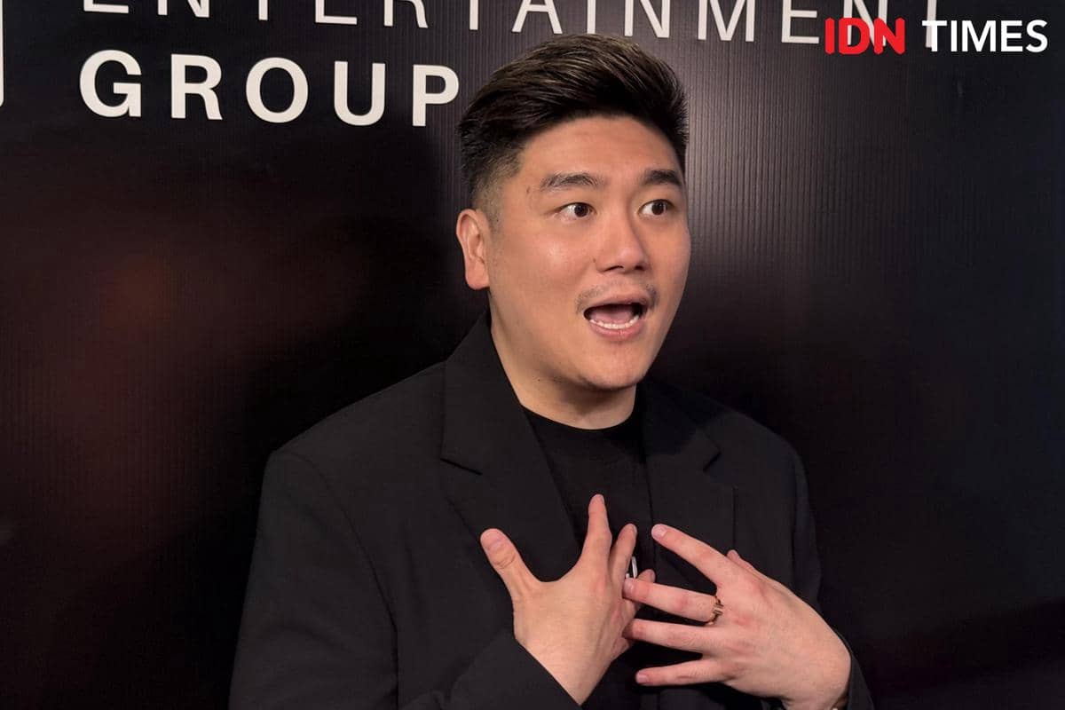Seorang pria mengenakan jas hitam berbicara dengan ekspresif di depan latar bertuliskan Entertainment Group.
