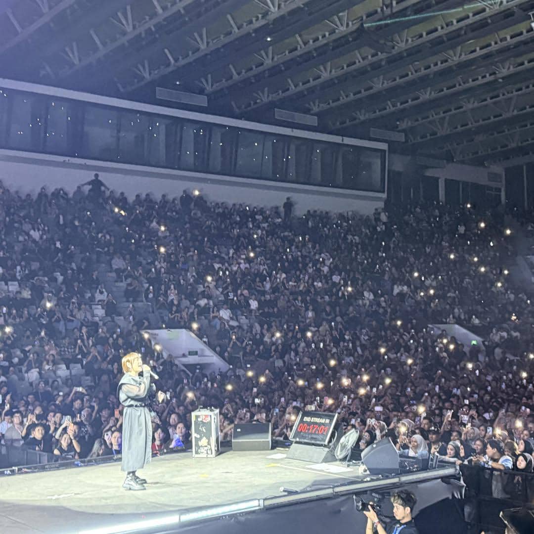 Seorang penyanyi tampil di atas panggung besar di depan penonton yang memenuhi arena konser dengan lampu ponsel menyala.