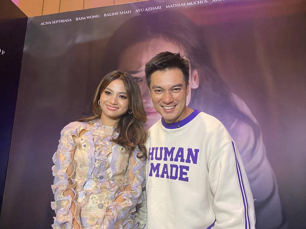 Dua orang berdiri berpose bersama di depan backdrop film Suamiku Lukaku saat konferensi pers di XXI Epicentrum, Jakarta.