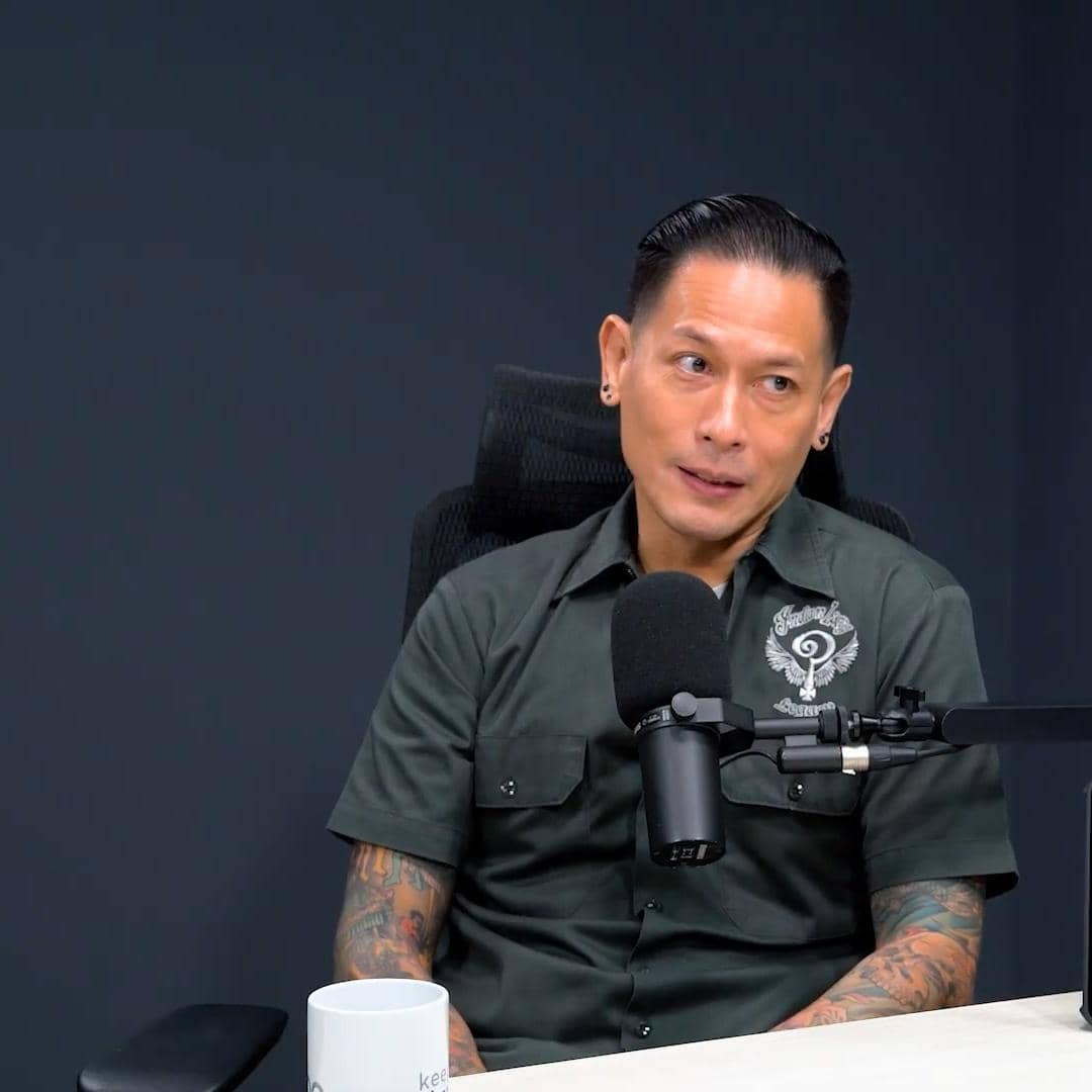 Seorang pria bertato mengenakan kemeja hijau duduk di depan mikrofon di studio dengan latar belakang gelap.