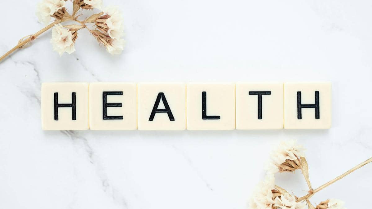 Tulisan HEALTH menggunakan balok mainan dengan latar belakang marmer putih dan bunga kering.