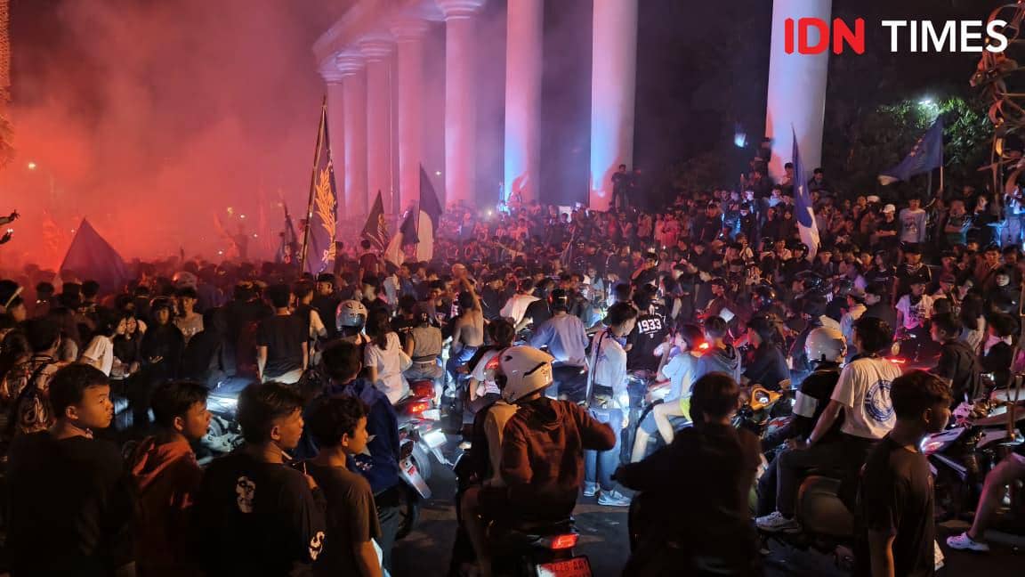 Ribuan orang berkumpul di sekitar Tugu Kujang Kota Bogor pada malam hari dengan suar merah dan bendera biru untuk merayakan kemenangan Persib.