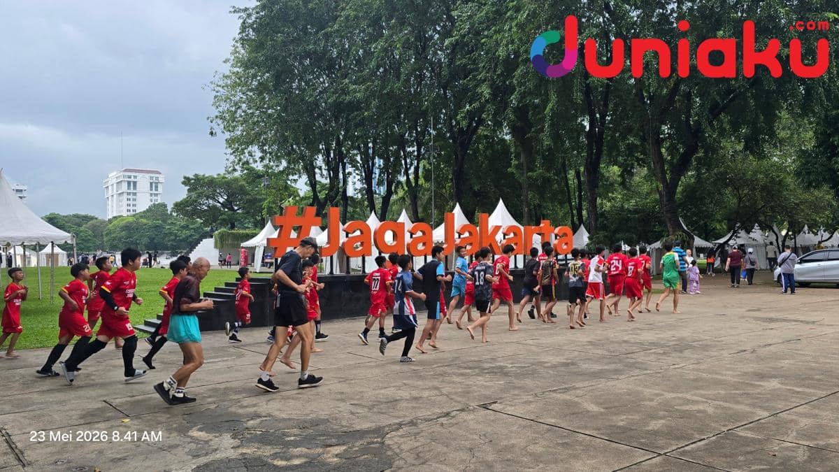 Sejumlah anak dan remaja berolahraga di Lapangan Banteng Jakarta dengan latar tulisan besar oranye #JagaJakarta dan tenda putih di sekitarnya.