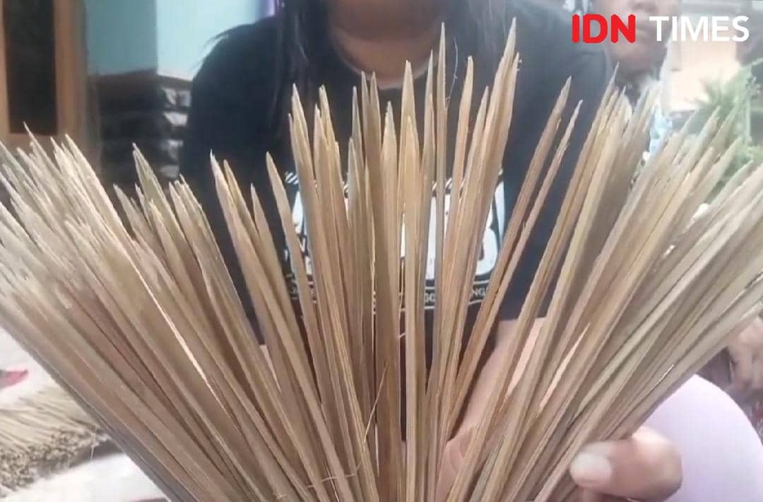 Perempuan memegang sapu lidi dari pelepah kelapa yang telah dikeringkan sebagai hasil kerajinan tangan rumahan.