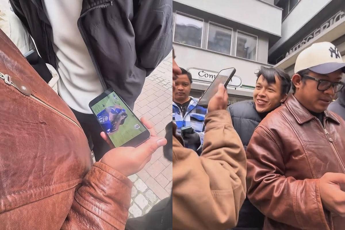 Sekelompok orang mengenakan jaket menonton pertandingan Persib Bandung melalui ponsel di area luar gedung.