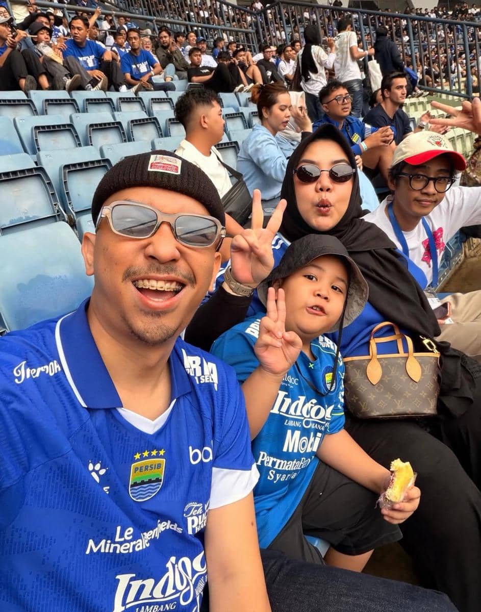 Suporter mengenakan jersey Persib Bandung berpose gembira di tribun stadion saat merayakan kemenangan tim di Super League Indonesia.