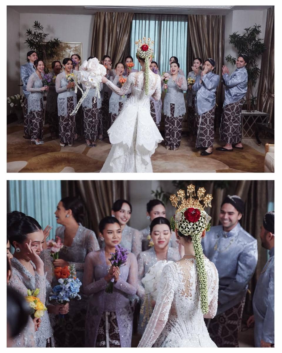 Pengantin wanita mengenakan kebaya putih dan siger emas dikelilingi para pengiring berpakaian kebaya abu-abu dalam suasana pernikahan adat.