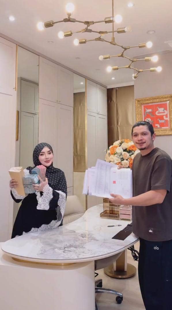 Seorang wanita berhijab memegang uang dan amplop bersama seorang pria yang memegang berkas di ruang kerja modern dengan dekorasi elegan.