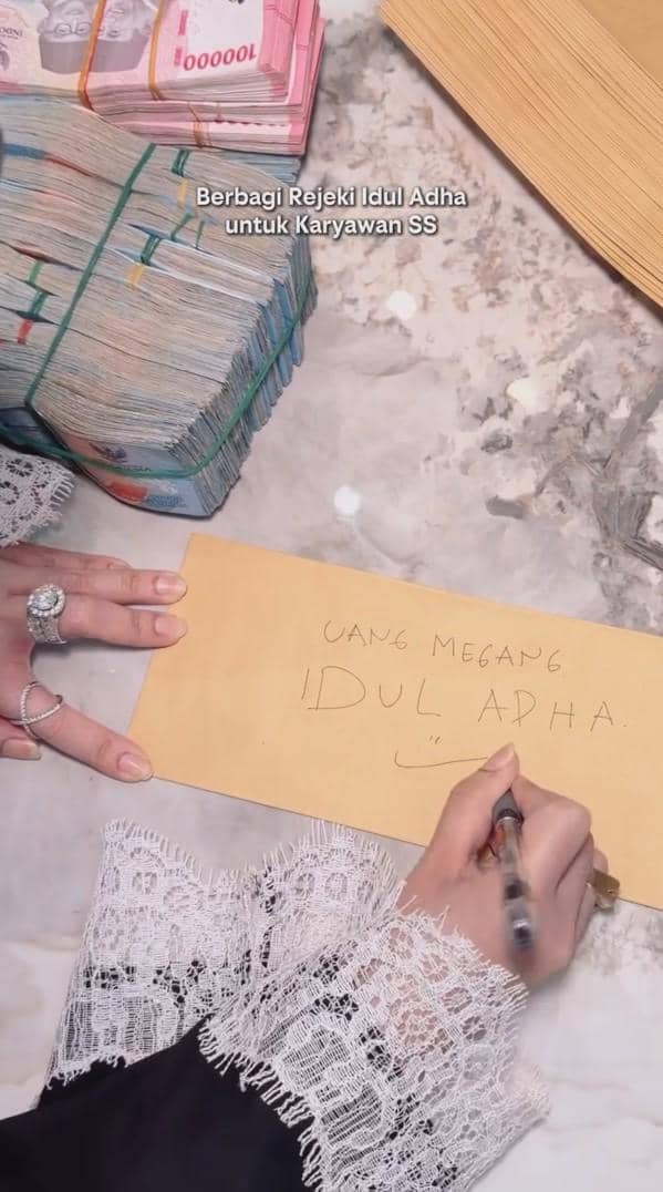 Seseorang menulis di amplop bertuliskan 'Uang Megang Idul Adha' di samping tumpukan uang pecahan rupiah untuk dibagikan sebagai THR.