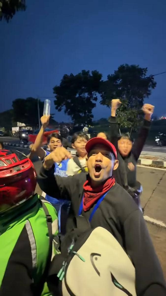 Sekelompok orang bersorak dan mengangkat tangan di jalan pada malam hari merayakan kemenangan Persib Bandung di Super League Indonesia.
