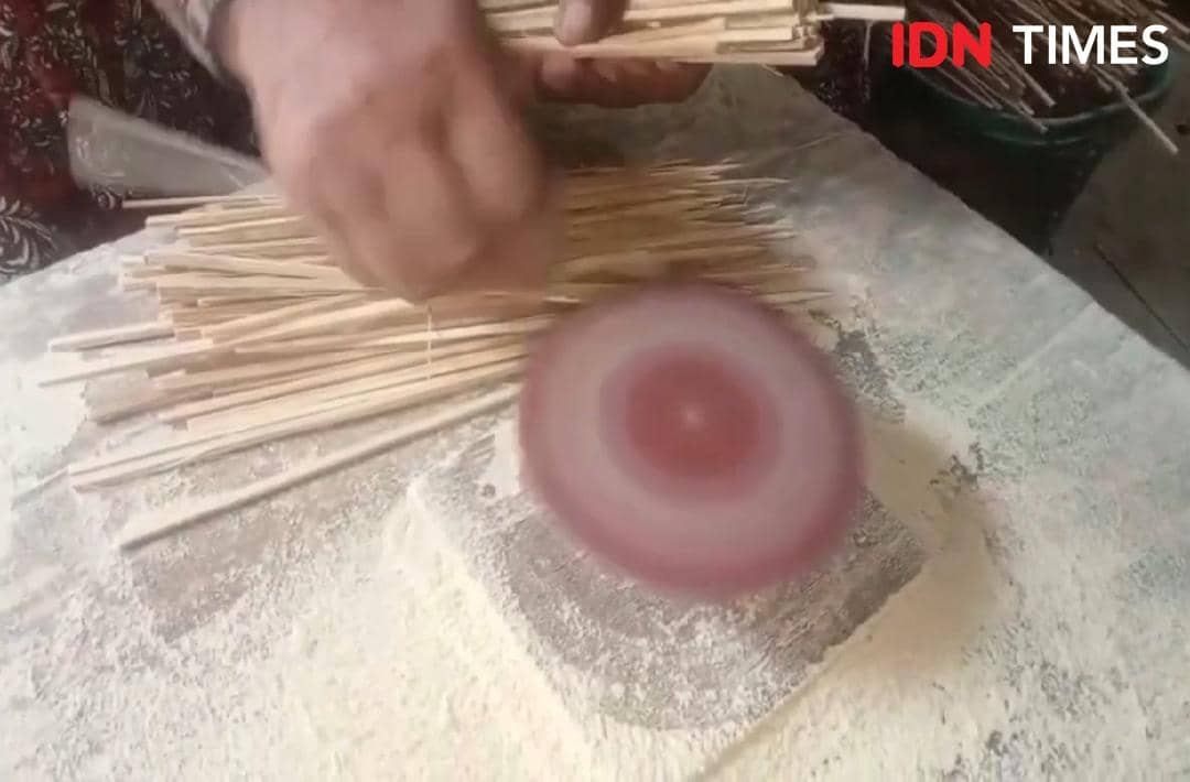 Seorang pengrajin menghaluskan tusuk sate bambu menggunakan alat pemutar di atas meja kerja menjelang perayaan Iduladha.