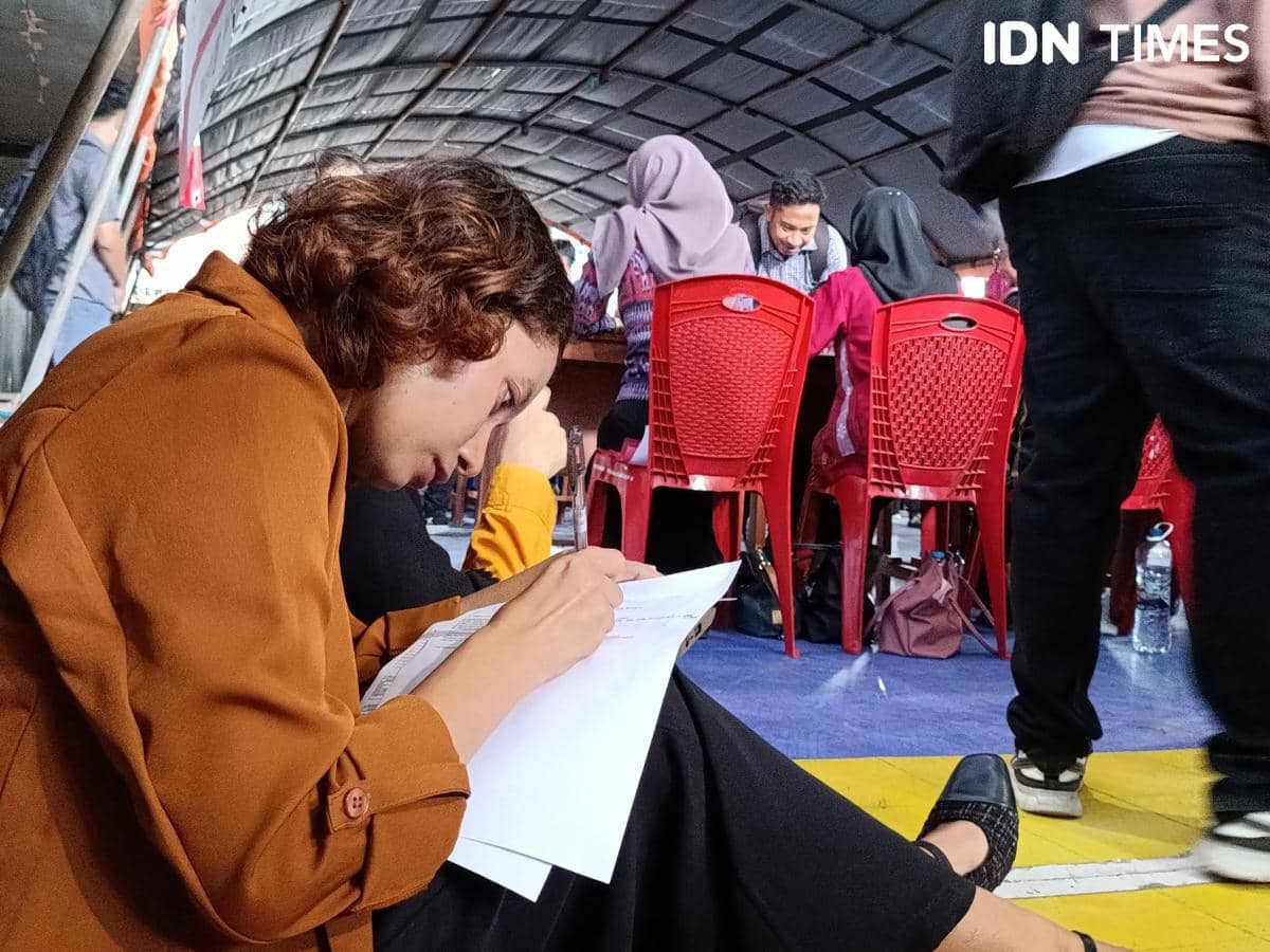 Seorang pencari kerja mengisi formulir lamaran di acara Job Fair NTT 2026 di Kupang dengan suasana ramai di sekitar area pendaftaran.