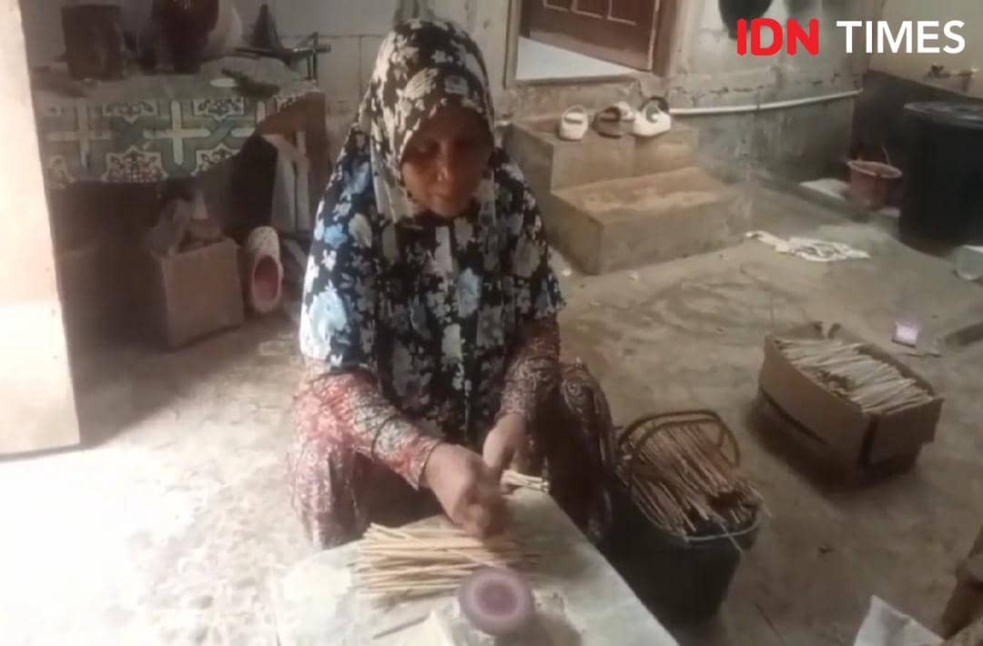 Seorang perempuan mengenakan kerudung bermotif sedang merapikan tusuk sate di dalam rumah sederhana di Patikraja, Banyumas.