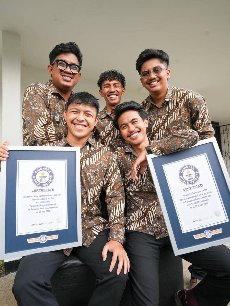 Lima pria mengenakan batik cokelat tersenyum sambil memegang dua sertifikat Guinness World Records di sebuah ruangan terbuka.