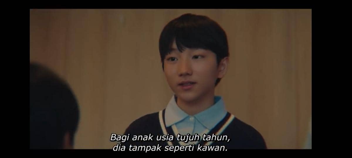 Seorang anak laki-laki mengenakan kemeja biru dan sweater gelap sedang berbicara dalam cuplikan drama Korea My Royal Nemesis di Netflix.
