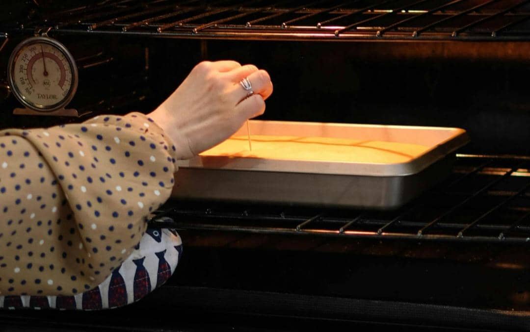 Seseorang melakukan tes tusuk pada adonan kue di dalam oven menggunakan tusuk gigi untuk memeriksa tingkat kematangan kue.