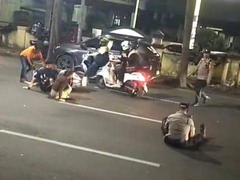 Beberapa petugas kepolisian dan warga berada di jalan setelah insiden tabrakan antara pengendara motor dan petugas saat razia malam di Makassar.