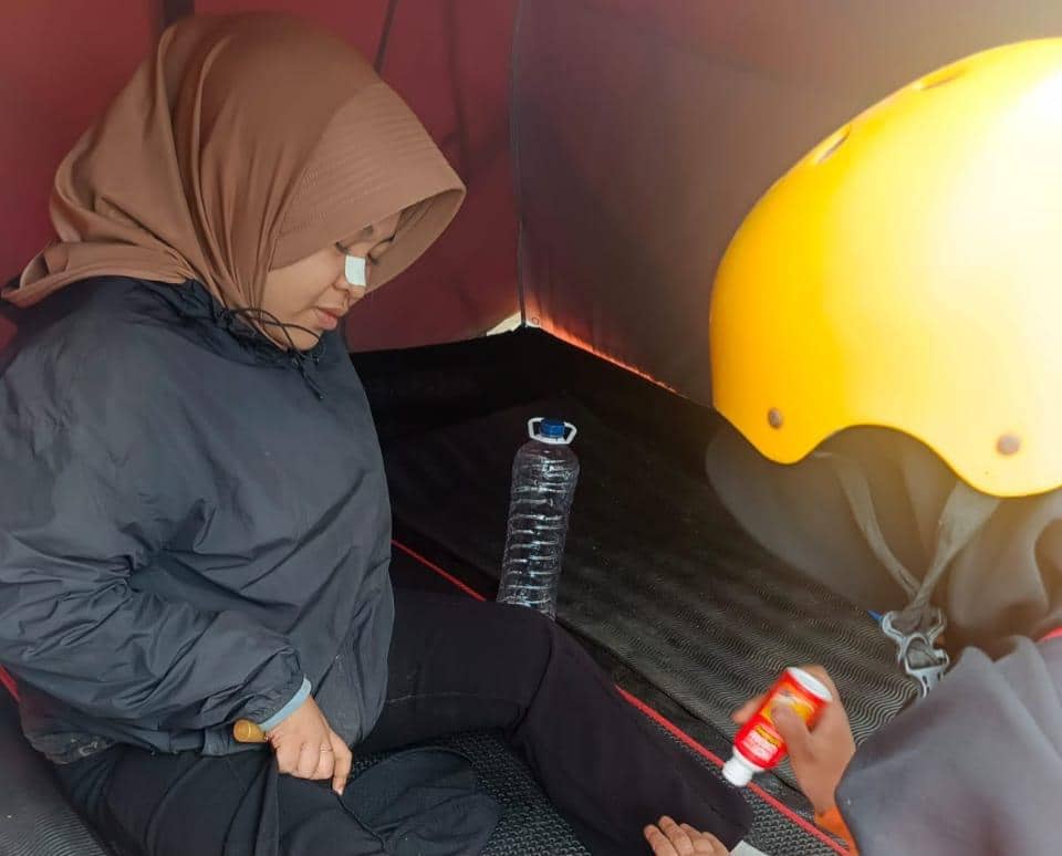 Seorang pendaki perempuan duduk di dalam tenda mendapat pertolongan dari anggota SAR yang mengenakan helm kuning di Gunung Bulubaria.