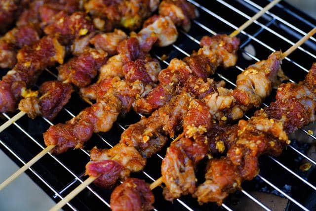Beberapa tusuk sate kambing berlemak sedang dipanggang di atas bara api dengan bumbu rempah yang menggugah selera.