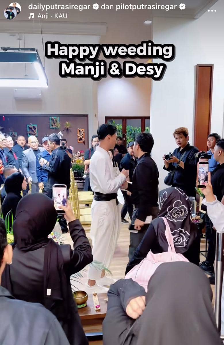Suasana pernikahan dengan pasangan pengantin dan para tamu yang hadir di ruangan tertutup, beberapa orang mengambil foto dan video.