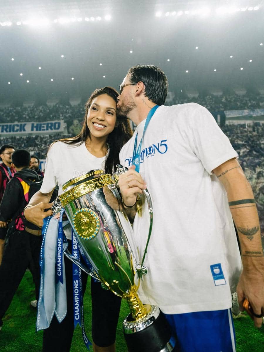 Seorang pemain Persib Bandung mencium pasangannya sambil memegang trofi juara di stadion yang dipenuhi penonton.