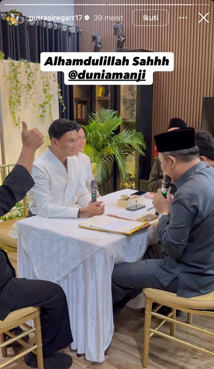Pasangan pengantin mengenakan busana putih duduk di depan penghulu saat prosesi akad nikah di ruangan yang dihiasi tanaman hijau.