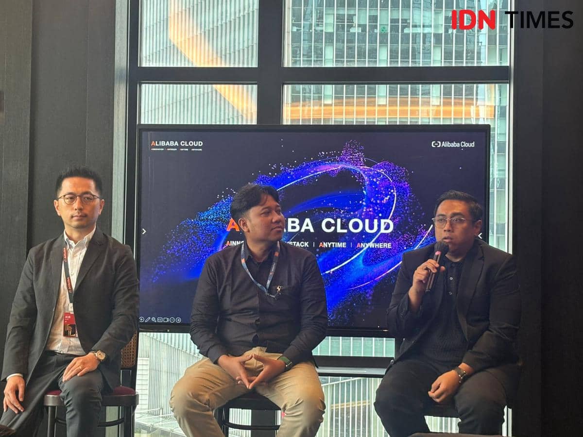 Tiga pria duduk di depan layar bertuliskan Alibaba Cloud saat konferensi pers media di Jakarta dengan latar gedung perkantoran modern.